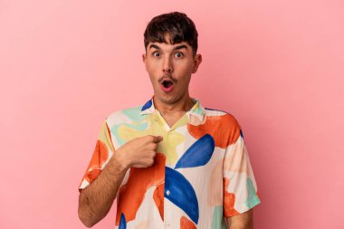 Pembe arka planda izole edilmiş genç bir ırk. Parmakla göstererek şaşırmış, geniş bir gülümsemeyle..