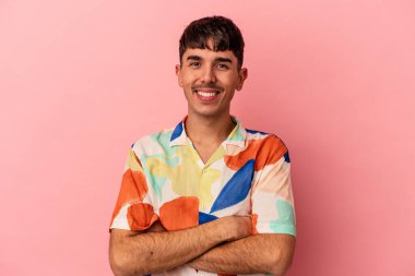 Pembe arka planda soyutlanmış, kendinden emin, kararlılıkla kollarını kavuşturan genç melez bir adam..