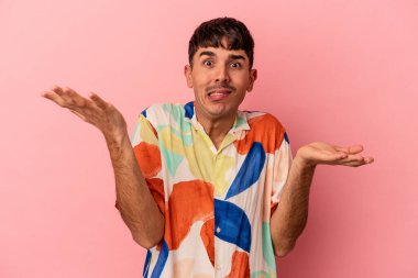 Genç melez adam pembe arka planda izole edilmiş. Kafası karışmış ve omuz silkiyor. Kopya alanını tutmak için..