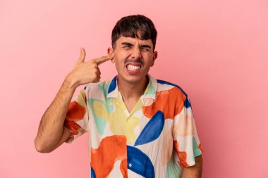 Genç melez adam pembe arka planda izole edilmiş kulakları elleriyle kapatıyor..