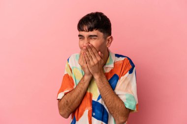 Genç melez adam pembe arka planda izole edilmiş bir şekilde bir şeylere gülüyor, ağızlarını ellerle kapatıyor..
