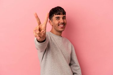 Genç melez adam pembe arka planda izole edilmiş neşeli ve tasasız parmakları olan bir barış sembolü gösteriyor..