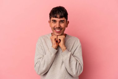 Pembe arka planda izole genç melez adam ellerini çenesinin altında tutuyor, mutlu bir şekilde yana bakıyor..