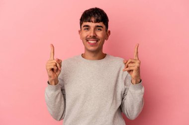 Pembe arka planda izole genç melez adam iki ön parmağı da boş bir alan gösteriyor..