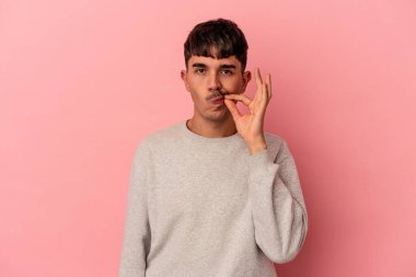 Genç melez adam pembe arka planda izole edilmiş, parmakları dudaklarında bir sır saklıyor..