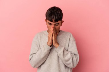 Genç melez adam pembe arka planda izole edilmiş dua ediyor, bağlılık gösteriyor, dindar biri ilahi ilham arıyor..