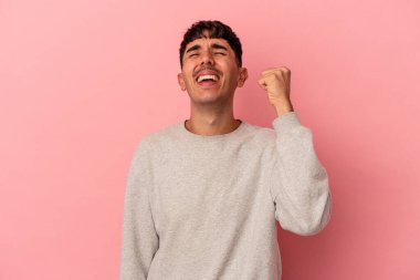 Genç melez adam pembe arka planda izole edilmiş zaferi, tutkuyu ve coşkuyu kutluyor, mutlu bir ifade..