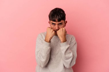 Genç melez bir adam pembe arka planda izole edilmiş. Yumruk atıyor, sinirleniyor, kavga ediyor..