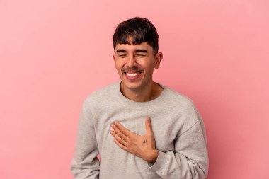 Pembe arka planda soyutlanmış genç melez adam yüksek sesle gülüyor elini göğsünde tutuyor..