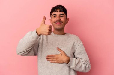 Genç melez adam pembe arka planda izole edilmiş karnına dokunuyor, nazikçe gülümsüyor, yemek yiyor ve tatmin oluyor..