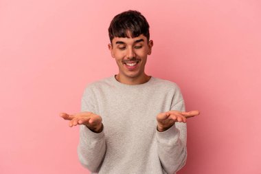 Genç melez adam pembe arka planda izole edilmiş. Elinde avuç içi olan bir şeyle kameraya sunuyor..