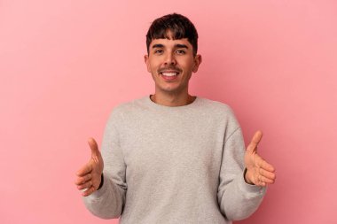 Genç melez adam pembe arka planda izole edilmiş iki elle bir şey tutuyor, ürün sunumu..