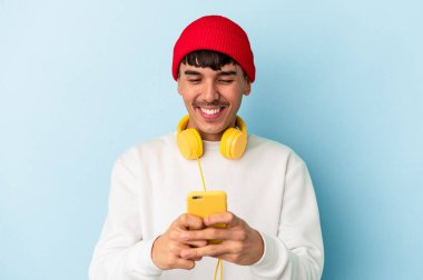 Genç melez adam mavi arka planda izole edilmiş müzik dinliyor.