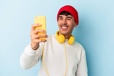 Genç melez adam mavi arka planda izole edilmiş müzik dinliyor.