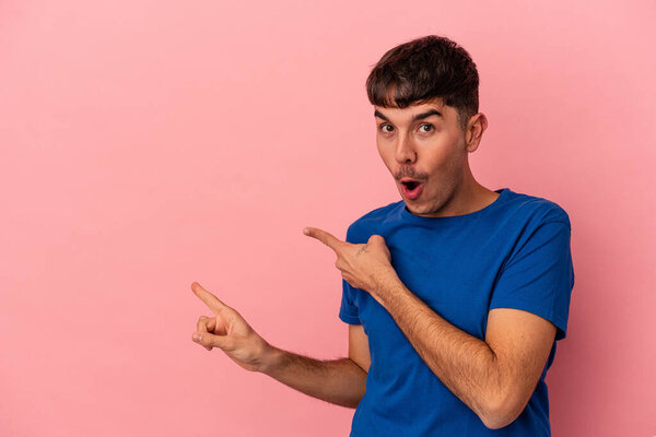 Молодой человек смешанной расы изолирован на розовом фоне, указывая указательными пальцами на пространство для копирования, выражая восхищение и желание.