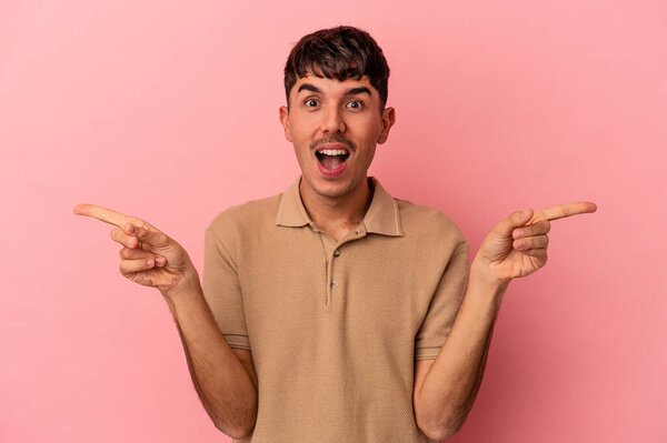 Молодой человек смешанной расы выделяется на розовом фоне, указывая на разные места для копирования, выбирая одно из них, показывая пальцем.