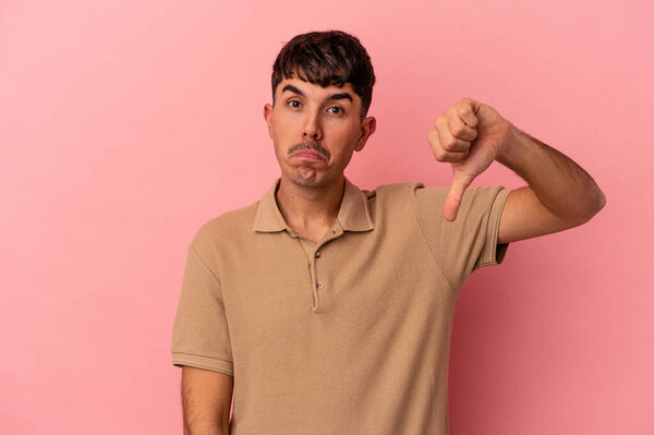 Молодой человек смешанной расы, изолированный на розовом фоне, показывает неприязненный жест, пальцы вниз. Концепция разногласий.