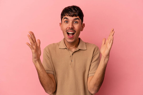 Молодой человек смешанной расы, изолированный на розовом фоне, получающий приятный сюрприз, возбужденный и поднимающий руки.