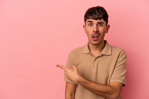 Молодой смешанной расы человек изолирован на розовом фоне указывая в сторону