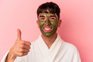 Güzellik maskesi takan melez genç bir adam pembe arka planda izole edilmiş.