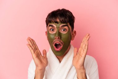 Güzellik maskesi takan melez genç bir adam pembe arka planda izole edilmiş.