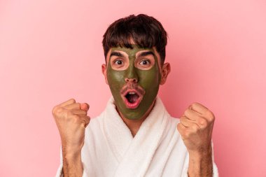 Güzellik maskesi takan melez genç bir adam pembe arka planda izole edilmiş.