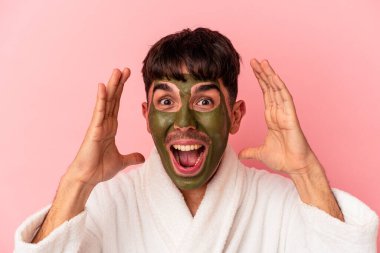 Güzellik maskesi takan melez genç bir adam pembe arka planda izole edilmiş.