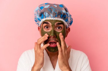 Güzellik maskesi takan melez genç bir adam pembe arka planda izole edilmiş.