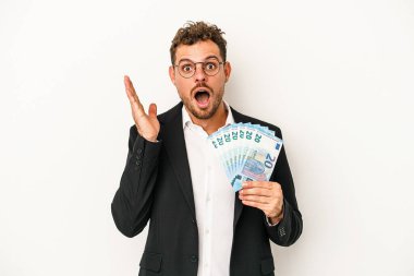 Beyaz arka planda banknotlar tutan genç beyaz adam şaşırdı ve şok oldu..