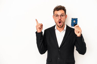 Beyaz arka planda HDD tutan beyaz bilgisayarlı genç adam yan tarafı işaret ediyor