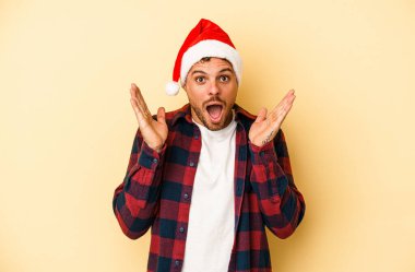 Sarı arka planda izole edilmiş, şaşırmış ve şok olmuş genç beyaz bir adam Noel 'i kutluyor..