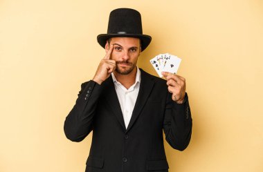 Kafkas büyücüsünün elinde sihirli bir kart var. Sarı arka planda izole edilmiş. Şakağı işaret ediyor, düşünüyor ve bir göreve odaklanıyor..