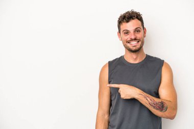 Beyaz arka planda izole edilmiş genç beyaz bir adam gülümsüyor ve boş alanda bir şeyler gösteriyor..