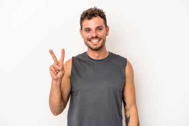 Beyaz arka planda izole edilmiş genç beyaz bir adam zafer işareti gösteriyor ve gülümsüyor..