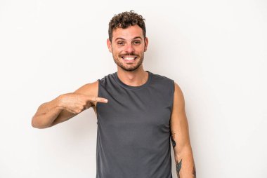 Beyaz arka planda yaşayan beyaz tenli genç bir adam gömlek fotokopi alanını gösteriyor, gururlu ve kendinden emin.