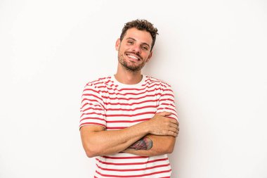 Beyaz arka planda kendini güvende hisseden, kararlılıkla kollarını kavuşturan beyaz tenli genç bir adam..