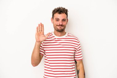 Beyaz arka planda izole edilmiş genç beyaz bir adam gülümseyerek beş numarayı parmaklarıyla gösteriyor..