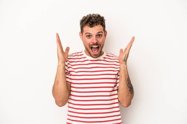 Beyaz arka planda izole olmuş genç beyaz bir adam zaferi veya başarıyı kutluyor, şaşırıyor ve şok oluyor..