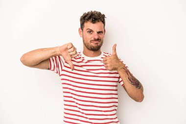 Beyaz arka planda izole edilmiş genç beyaz bir adam baş parmaklarını aşağı ve yukarı kaldırıyor, zor seçim konsepti