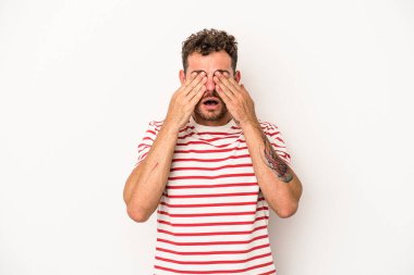 Beyaz arka planda izole edilmiş genç beyaz bir adam elleriyle gözlerini kapatmaktan korkuyor..