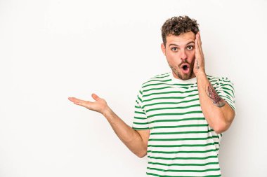 Beyaz arka planda izole edilmiş genç beyaz adam, avuç içi fotokopi alanını elinde tutmaktan etkilenmiş..