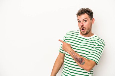 Beyaz arka planda izole edilmiş genç beyaz bir adam gülümsüyor ve boş alanda bir şeyler gösteriyor..