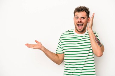 Beyaz arka planda izole edilmiş genç beyaz bir adam bir avuç içinde fotokopi alanı tutuyor, el üstünde tutuyor. Şaşırmış ve mutlu..