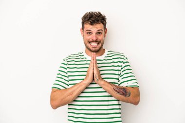 Beyaz arka planda izole edilmiş genç beyaz bir adam el ele tutuşup, ağız kenarında dua ediyor, kendinden emin..