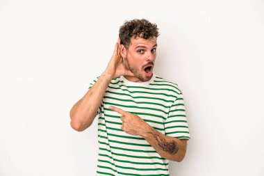 Beyaz arka planda izole edilmiş genç beyaz adam bir dedikoduyu dinlemeye çalışıyor..