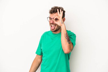 Beyaz arka planda izole genç beyaz adam heyecanlı tamam göz jesti tutmak.