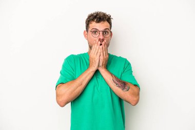 Beyaz arka planda izole edilmiş genç beyaz adam elleriyle ağzını kapatırken şok oldu..