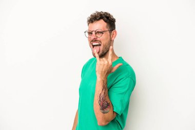 Beyaz arka planda izole edilmiş genç beyaz bir adam parmaklarıyla kaya hareketi gösteriyor.