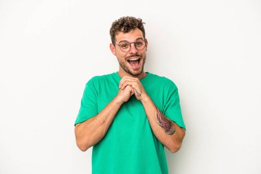 Beyaz arka planda izole edilmiş genç beyaz bir adam şans için dua ediyor, şaşırmış ve ağzını açıp önüne bakıyor..