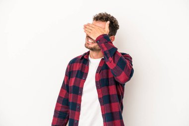 Beyaz arka planda soyutlanmış beyaz tenli genç bir adam elleriyle gözlerini kapatıyor, geniş bir gülümsemeyle bir sürpriz bekliyor..